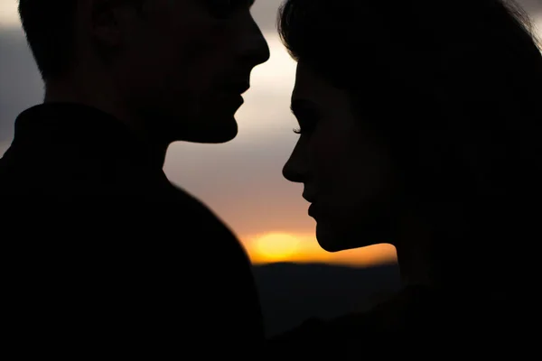 Silhouet liefhebbers bij zonsondergang. Silhouetten van een jong koppel geliefden bij zonsondergang in stralen van ondergaande zon. — Stockfoto