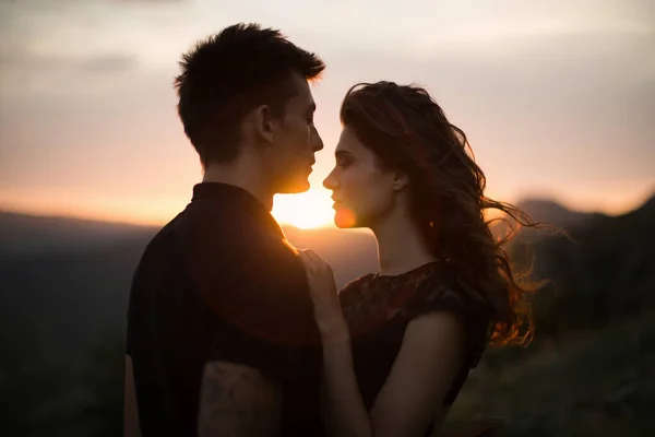 Amantes da silhueta ao pôr-do-sol. Silhuetas de um jovem casal amantes ao pôr do sol em raios de pôr do sol . — Fotografia de Stock