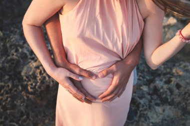 Zarif pembe elbiseli hamile bir kadının göbeğine elleriyle dokunduğu fotoğrafı kapat..