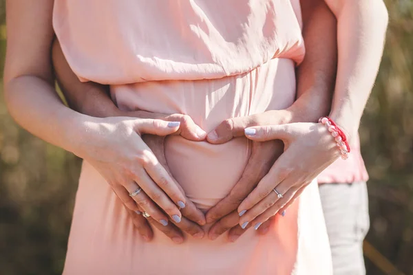 Close-up foto van jonge zwangere vrouw in elegante roze jurk aanraken van haar buik met handen. — Stockfoto