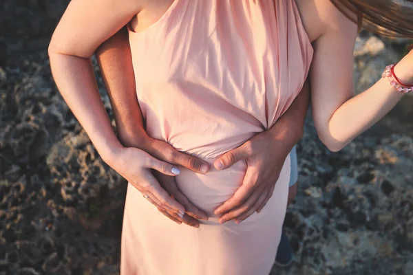 Nahaufnahme Foto einer jungen Schwangeren in elegantem rosa Kleid, die ihren Bauch mit den Händen berührt. — Stockfoto