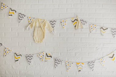 Stüdyoda beyaz taş bir duvara asılı bir bebeğin bayrakları ve kıyafetleri..