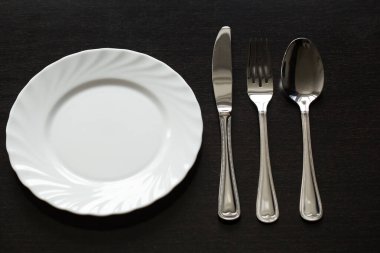 Siyah arka planda çatal bıçak takımı. Çatal, kaşık, bıçak, tabak.