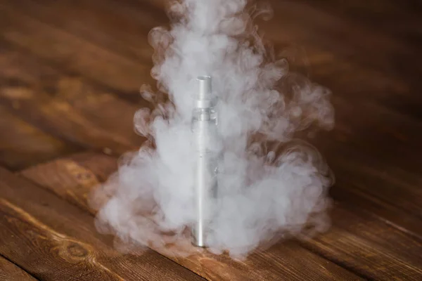 Cigarette électronique sur une table en bois. Fumée . — Photo