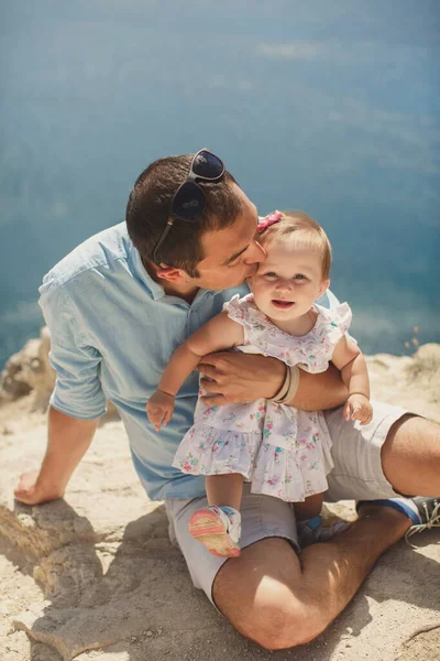Dad kisses daughter against the backdrop of mountains and the sea. — Stock Photo, Image