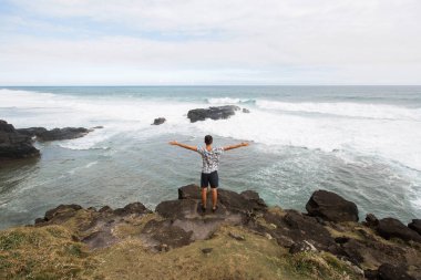 Dağın zirvesinde, okyanusa bakan mutlu bir adam. Başarı, kazanan, mutluluk..