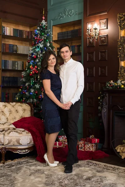 Hombre y mujer tomados de la mano cerca del árbol de Navidad y la chimenea en el ambiente navideño . — Foto de Stock