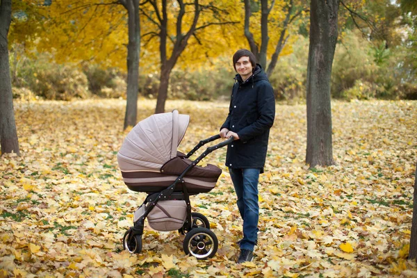Jovem caminhando em um parque de outono com um carrinho de bebê — Fotografia de Stock