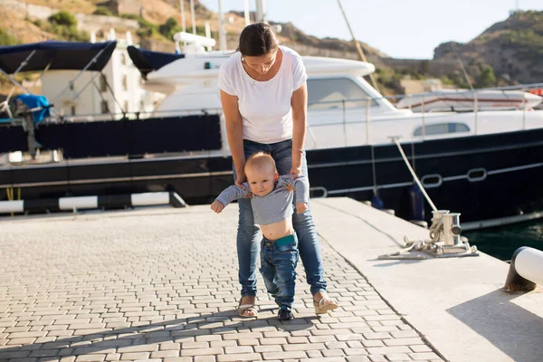 Mooie moeder is wandelen op de pier met haar kleine jongen zoon met eerste stappen — Stockfoto