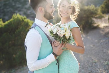Gelin ve damat su kenarındaki dağlarda doğada. Takım elbise ve kıyafet rengi Tiffany. Öp ve sarıl.