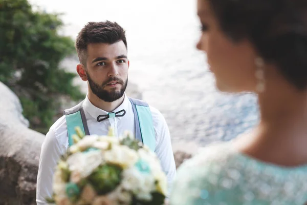 A noiva e o noivo na natureza nas montanhas perto da água. Terno e vestido Tiffany cor. O noivo olha para a distância . — Fotografia de Stock