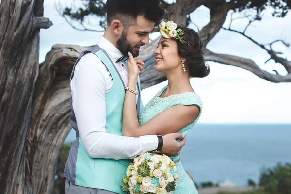 A noiva e o noivo na natureza nas montanhas perto da água. Terno e vestido Tiffany cor. Beijo e abraço . — Fotografia de Stock