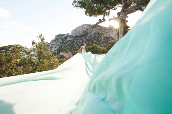 Menyasszony a természetben a hegyekben a víz közelében. Ruha színe Tiffany. A menyasszony játszik a ruhájával.. — Stock Fotó