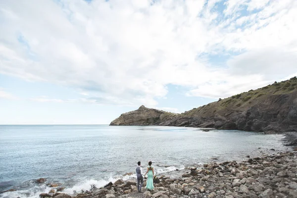 A noiva e o noivo na natureza nas montanhas perto da água. Terno e vestido Tiffany cor. Fique na praia de mãos dadas . — Fotografia de Stock