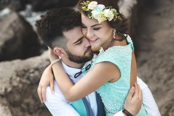 La novia y el novio en la naturaleza en las montañas cerca del agua. Traje y vestido de color Tiffany. Beso y abrazo . —  Fotos de Stock