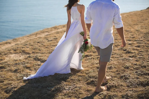 Bela jovem casal caminha ao longo do oceano ao pôr do sol . — Fotografia de Stock