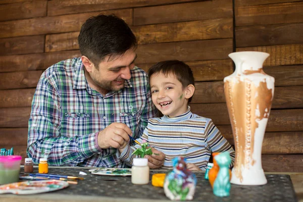 Father and son paint colors against a wooden wall.