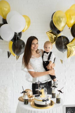 Anne ve oğul birlikte 1. doğum gününü kutluyorlar. Balonlarla gülüp gülüyorlar. Çikolata gibi..