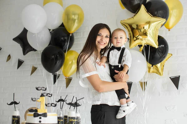 Anne ve oğul birlikte 1. doğum gününü kutluyorlar. Balonlarla gülüp gülüyorlar. Çikolata gibi..