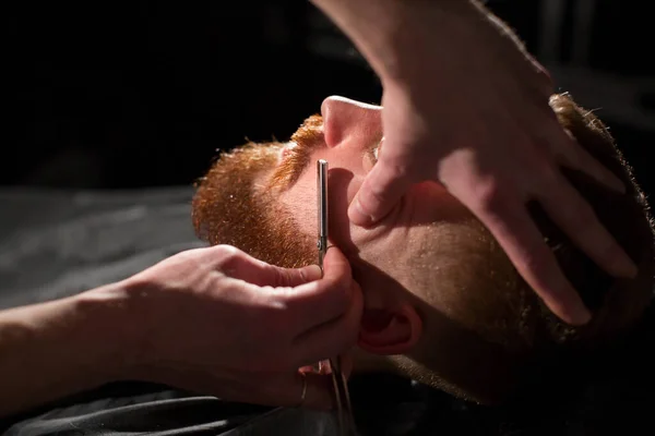 Il parrucchiere sta radendo la barba maschile con il coltello. bello barbuto uomo è ottenere rasato da parrucchiere a il barbiere . — Foto Stock