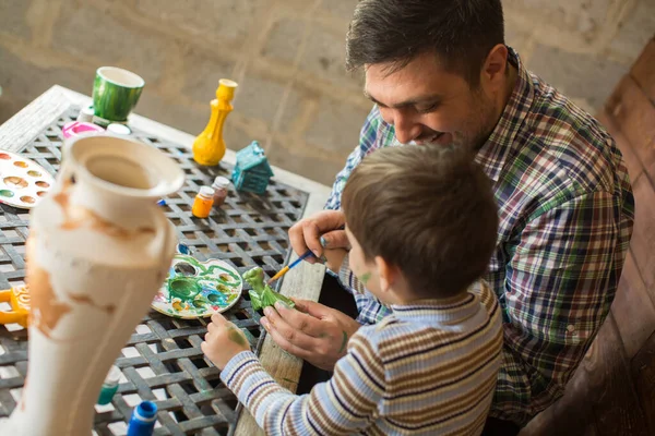 Father and son paint colors against a wooden wall.