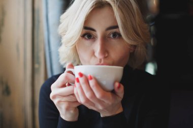 Güzel bir kadın beyaz bardaktan kahve içiyor..