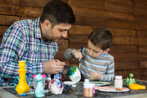 Father and son draw against a wooden wall.