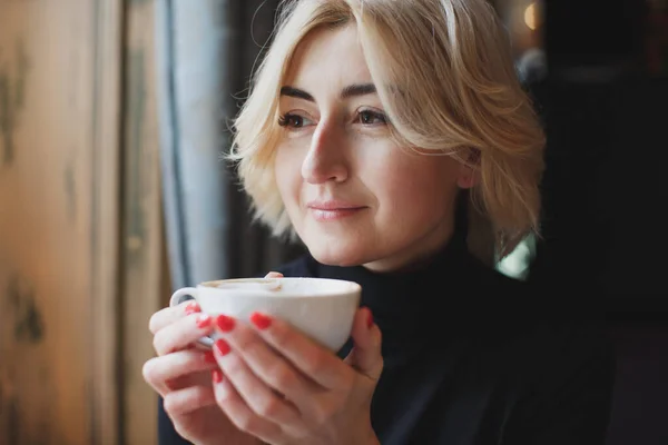 Una hermosa mujer bebe café de una taza blanca . — Foto de Stock