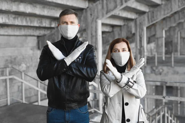 Un uomo e una donna mascherati mostrano un segnale di stop per il coronavirus. Il merluzzo bianco pandemico 202019. Ferma il coronavirus. Quarantena. Vaccino al coronavirus — Foto Stock
