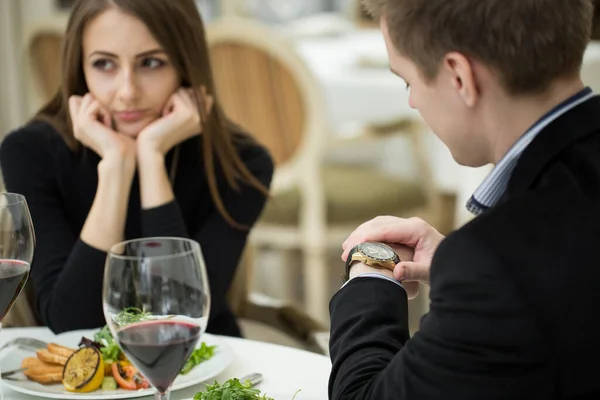 Молодая женщина делает раздражительный жест на плохом свидании в ресторане. Мужчина смотрит на часы . — стоковое фото