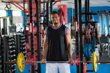 Spor salonundaki ağırlık odasında ağırlık kaldıran formda bir adam..