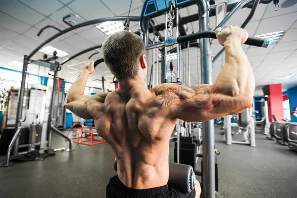 El hombro tira de la máquina. Hombre de fitness haciendo ejercicio en el gimnasio. Ejercicio de fuerza en la parte superior de la espalda . — Foto de Stock