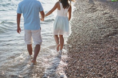 Denizin kenarındaki çakıl taşlarında el ele tutuşan çift.
