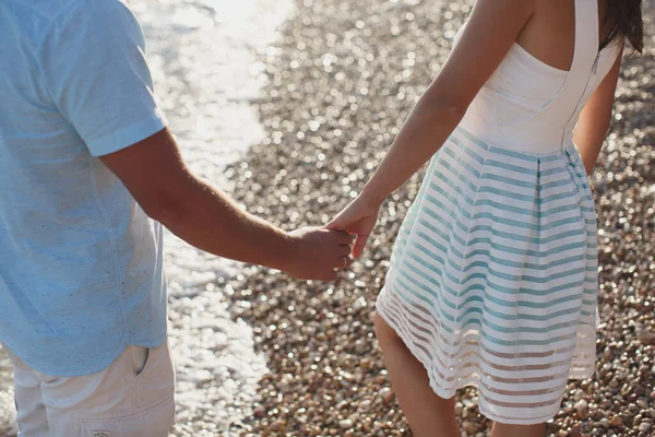 Pareja cogida de la mano caminando sobre los guijarros cerca del mar —  Fotos de Stock