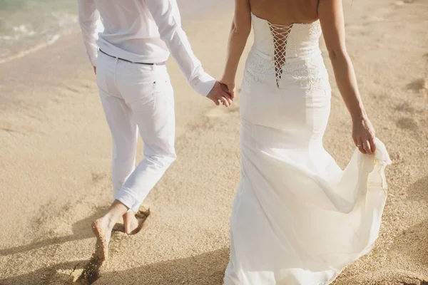 Braut und Bräutigam gehen Hand in Hand in den Sand. Fußabdrücke im Sand in der Nähe des Ozeans. — Stockfoto