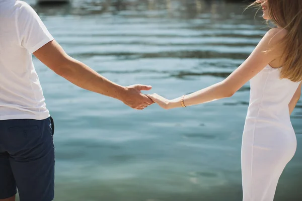 Junges Paar Junge und Mädchen weißes Kleid Händchen haltend auf dem Hintergrund des Wassers. — Stockfoto