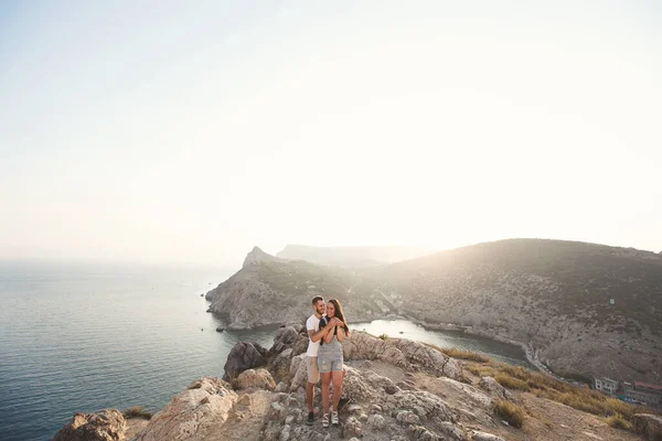 Szeretők, fiúk és lányok, a szikla szélén, a hegyek és óceánok hátterében — Stock Fotó