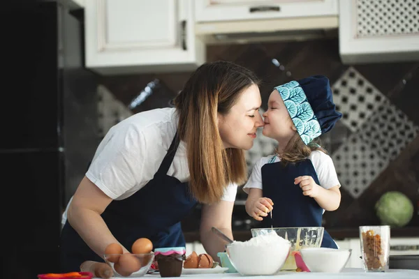 Genç anne ve kız mutfakta kek hazırlıyor ve kız annesini öpüyor. — Stok fotoğraf