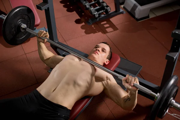Brutal athletic man pumping up muscles on bench press. — Stock Photo, Image