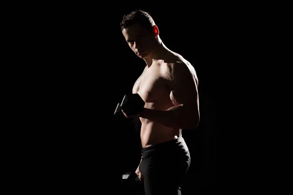 Όμορφος αθλητικός τύπος bodybuilder κάνει ασκήσεις με dumbbell. Γυμναστήριο μυϊκό σώμα σε σκούρο φόντο. — Φωτογραφία Αρχείου