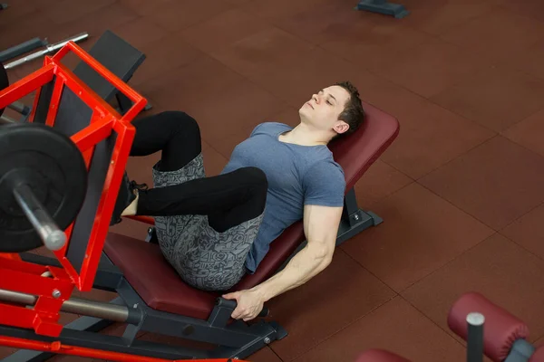 Atractivo joven haciendo la prensa de la pierna en la máquina en el gimnasio . — Foto de Stock