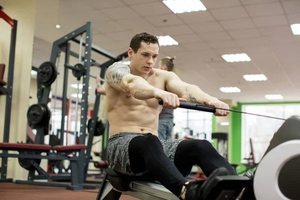 Man die roeioefeningen doet in de sportschool. — Stockfoto