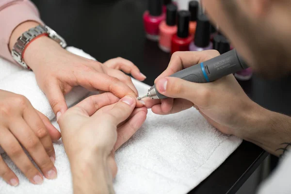 Mistrz używa maszyny elektrycznej do usuwania lakieru do paznokci podczas manicure w salonie. Manicure sprzętowy. Pojęcie pielęgnacji ciała — Zdjęcie stockowe