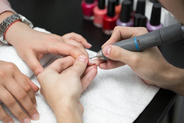 Mistrz używa maszyny elektrycznej do usuwania lakieru do paznokci podczas manicure w salonie. Manicure sprzętowy. Pojęcie pielęgnacji ciała — Zdjęcie stockowe