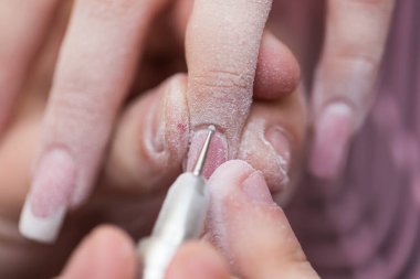 Ustanın yakın çekimi, kuaförde manikür yaparken ojeyi çıkarmak için elektrikli makine kullanıyor. Donanım manikürü. Vücut bakımı kavramı.