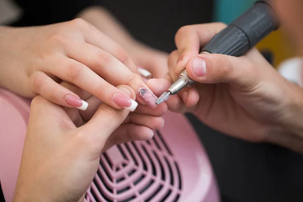 Ujęcie zbliżeniowe mistrza wykorzystuje elektryczną maszynę do usuwania lakieru do paznokci podczas manicure w salonie. Manicure sprzętowy. Pojęcie pielęgnacji ciała. — Zdjęcie stockowe