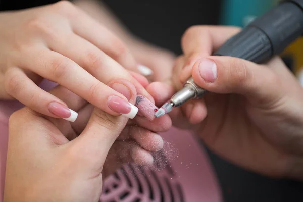Ujęcie zbliżeniowe mistrza wykorzystuje elektryczną maszynę do usuwania lakieru do paznokci podczas manicure w salonie. Manicure sprzętowy. Pojęcie pielęgnacji ciała. — Zdjęcie stockowe