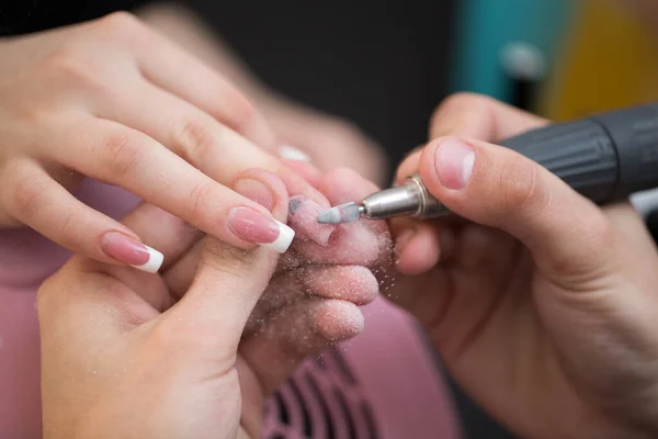 Ujęcie zbliżeniowe mistrza wykorzystuje elektryczną maszynę do usuwania lakieru do paznokci podczas manicure w salonie. Manicure sprzętowy. Pojęcie pielęgnacji ciała. — Zdjęcie stockowe