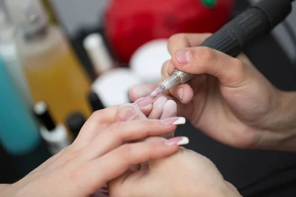 Ujęcie zbliżeniowe mistrza wykorzystuje elektryczną maszynę do usuwania lakieru do paznokci podczas manicure w salonie. Manicure sprzętowy. Pojęcie pielęgnacji ciała. — Zdjęcie stockowe