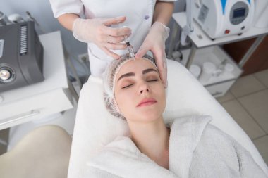 Kadın yüzüne iğne vuruluyor. Güzellik kraliçesi botoks yapıyor. Genç bir kadın kozmetoloji salonunda güzellik yüz enjeksiyonu yaptırıyor. Yaşlanma enjeksiyonuyla. Estetik Tıp, Kozmetoloji.